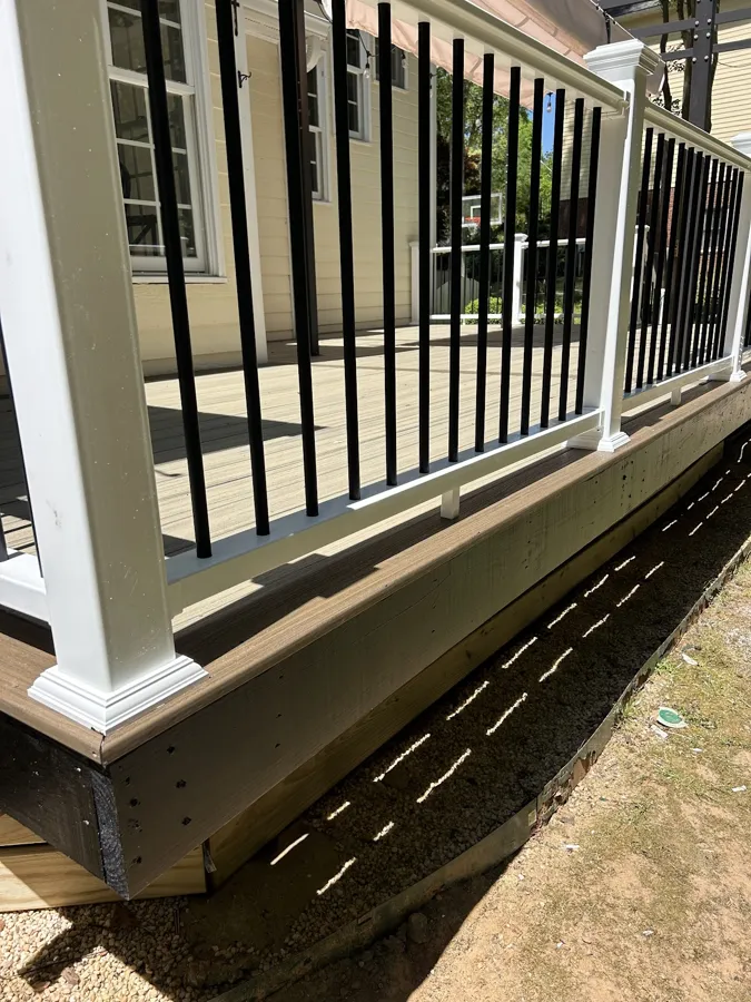 Composite deck boards with a white rail and black metal balusters, close up